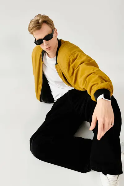 A young handsome man wears sunglasses and a mustard jacket while lounging in a relaxed pose. — Stock Photo