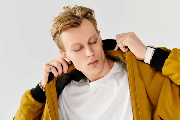 In a modern setting, a young man with striking features adjusts his jacket, exuding style. — Stock Photo