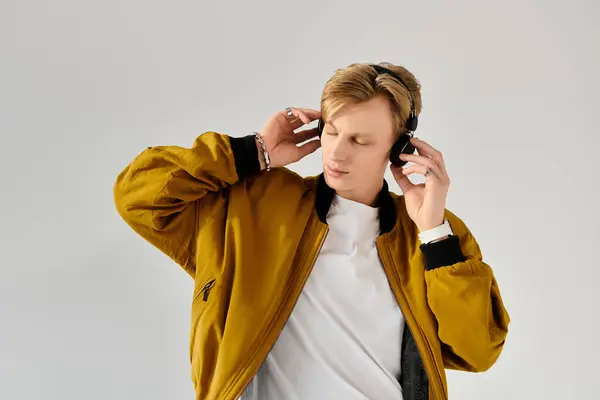 Joven con una chaqueta de moda y auriculares, perdido en la música contra un simple telón de fondo. - foto de stock