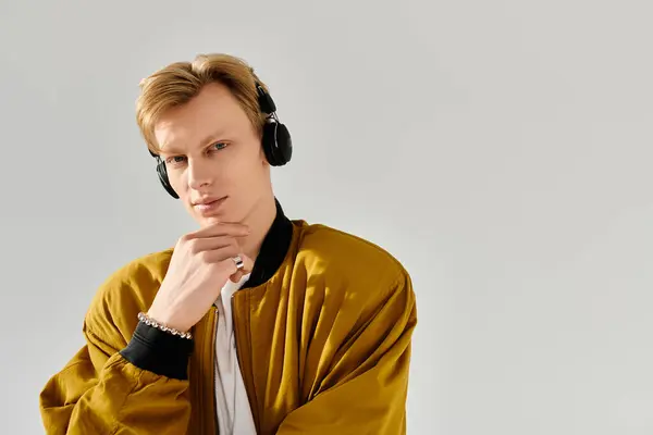 A confident young man in a stylish jacket listens to music against a plain backdrop. — Stock Photo