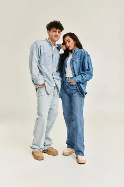 Fashionable duo poses in matching denim outfits, radiating confidence in a chic studio environment. — Stock Photo