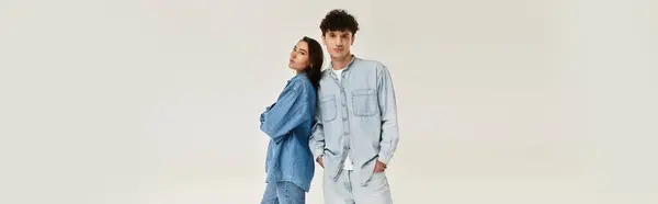 Jeune homme et femme posent avec confiance dans des tenues élégantes en denim dans un contexte minimaliste. — Photo de stock