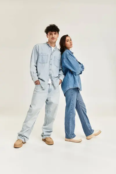 A fashionable pair stands back to back in stylish denim outfits, exuding confidence and charm. — Stock Photo