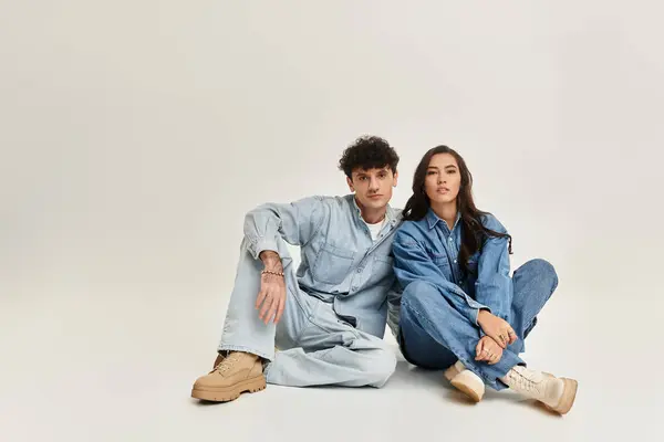 A young couple sits casually on the floor, dressed in matching denim outfits, radiating style. — Stock Photo