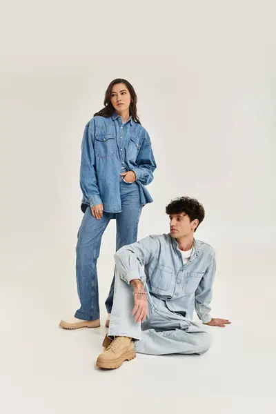 Two stylish individuals in trendy denim outfits pose elegantly in a minimalistic studio environment. — Stock Photo