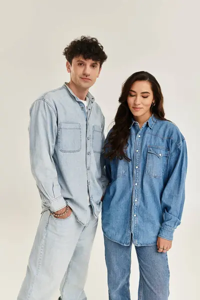A pair of young, fashionable individuals showcase their trendy denim outfits in a minimalist studio. — Stock Photo
