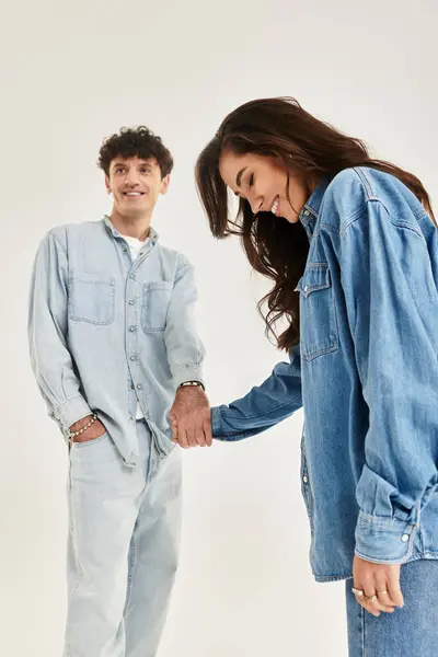 Two young individuals dressed in stylish denim, smiling and holding hands, exude confidence and joy. — Stock Photo
