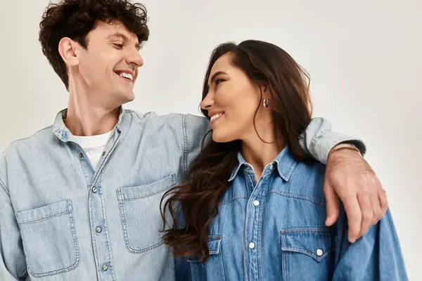 A trendy couple shares a warm smile, showcasing their stylish denim looks in a bright space. — Stock Photo