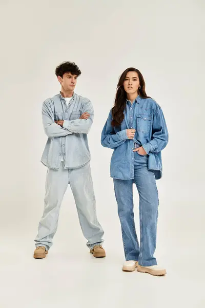 A stylish duo in relaxed denim poses confidently against a simple background, radiating youth. — Stock Photo