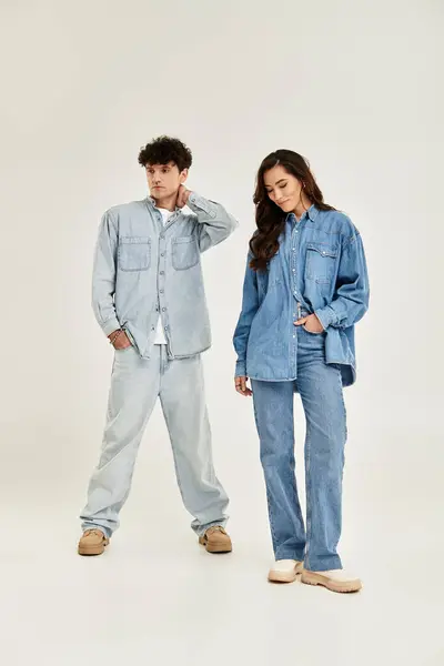 Young couple models fashionable denim outfits, exuding confidence in a bright studio. — Stock Photo