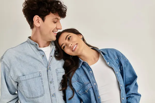 Una pareja joven de moda disfruta de un momento lúdico, sonriendo y abrazándose en trajes de mezclilla casuales. — Stock Photo