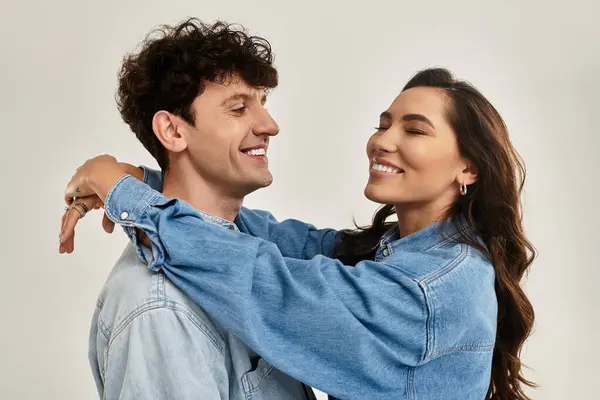 Charming young couple smiles and embraces while showcasing trendy denim attire in a light setting. — Stock Photo