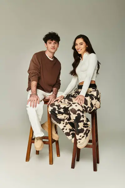 Una coppia alla moda seduta su sgabelli in legno, che presenta stili unici in un ambiente neutro e tonico. — Foto stock
