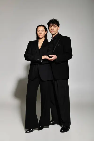 Young couple in trendy outfits stands confidently in a minimalist studio with soft lighting. — Stock Photo