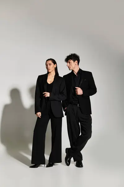 Dressed in chic black outfits, a young couple stands confidently against a soft backdrop. — Stock Photo