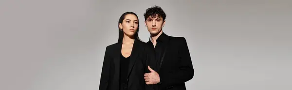 A fashion forward young couple pose confidently in tailored black outfits against a sleek backdrop. — Stock Photo