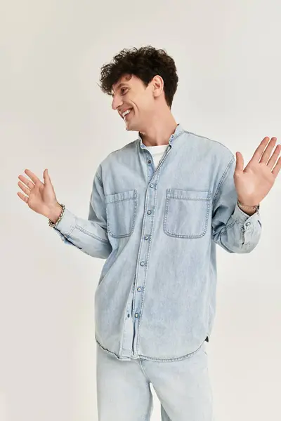 Un joven de moda se encuentra en un estudio brillante, expresando alegría mientras usa atuendo de mezclilla. - foto de stock