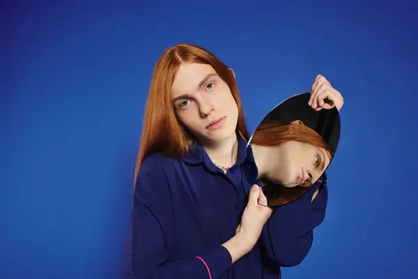 A young queer man with long red hair poses confidently while holding a reflective surface. — Fotografia de Stock