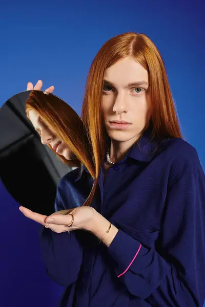 Eine stylische junge Person mit langen roten Haaren überprüft ihr Spiegelbild in einem runden Spiegel. — Stockfoto