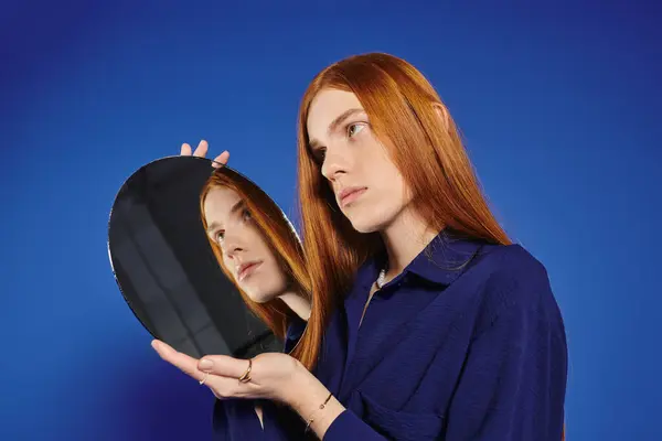 A young man with long red hair gazes into a round mirror, pondering self discovery. — Stock Photo