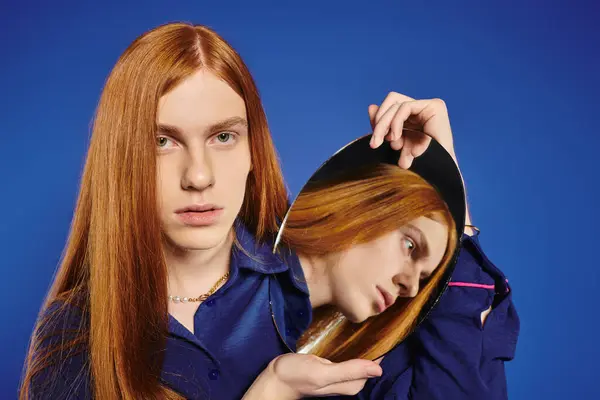 Queer youth with long red hair poses, reflecting on self identity in a mirror. — Stock Photo