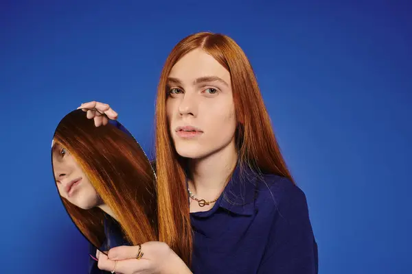 Ein junger Mann mit langen roten Haaren hält einen Spiegel, der sein modisches und künstlerisches Wesen widerspiegelt. — Stockfoto