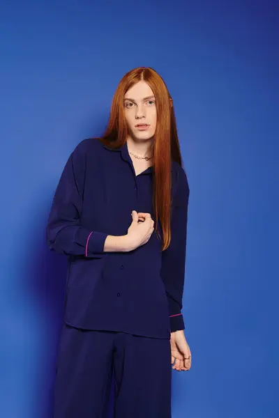 A stylish young man with striking red hair poses against a vibrant blue background. — Stock Photo