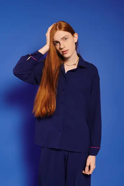 A young man with long red hair and a stylish outfit showcases his modern fashion against bold blue. — Stock Photo