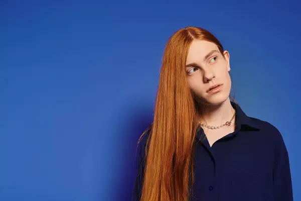 Um jovem queer elegante homem com cabelo longo vermelho apresenta um olhar moderno e postura cativante. — Fotografia de Stock