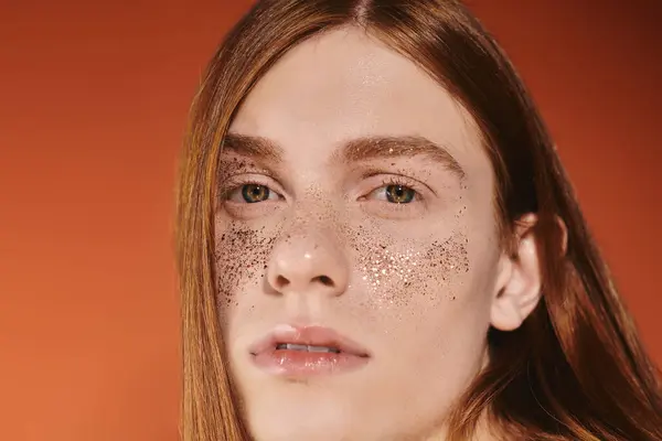 A young queer man showcases his red hair and bold makeup in warm lighting. — Stock Photo