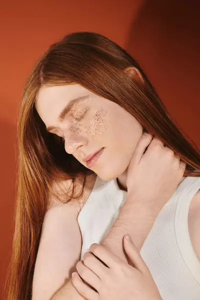 A fashionable young man with long red hair gazes peacefully while wearing glitter on his cheek. — Stock Photo