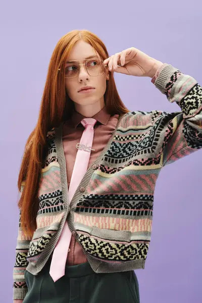 A stylish young man with red hair poses in a patterned cardigan and pink tie against purple. — Stock Photo