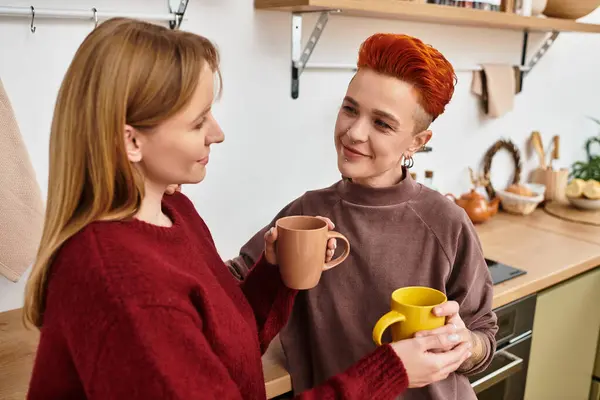 Due belle donne condividono una bevanda calda nella loro casa elegante, celebrando l'amore e la connessione. — Foto stock