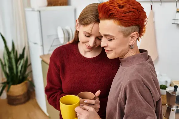 Zwei schöne Frauen umarmen sich bei warmen Getränken in ihrer modernen Wohnung voller Liebe. — Stockfoto