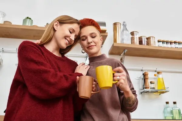 De belles jeunes femmes partagent un moment tendre dans leur cuisine élégante autour de boissons chaudes à la maison. — Photo de stock