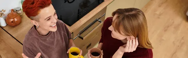 Дві молоді жінки діляться сміхом і кавою в своїй стильній квартирі, святкуючи любов, банер — стокове фото