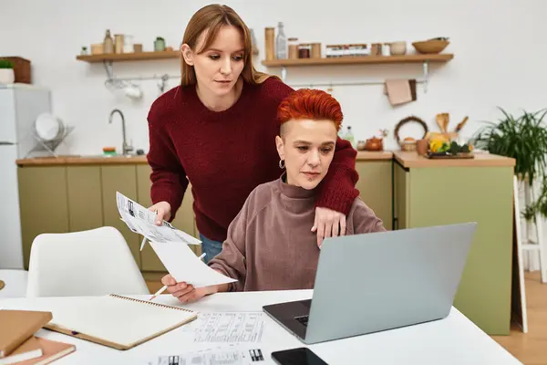 Zwei junge Frauen teilen einen zärtlichen Moment bei der gemeinsamen Arbeit in ihrem stilvollen Zuhause. — Stockfoto