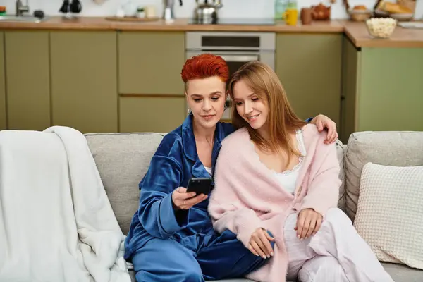 Two beautiful women relax together in their cozy apartment while enjoying each others company. — Stock Photo