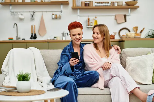 Two beautiful young women relax together on a comfortable couch in their stylish home. — Stock Photo