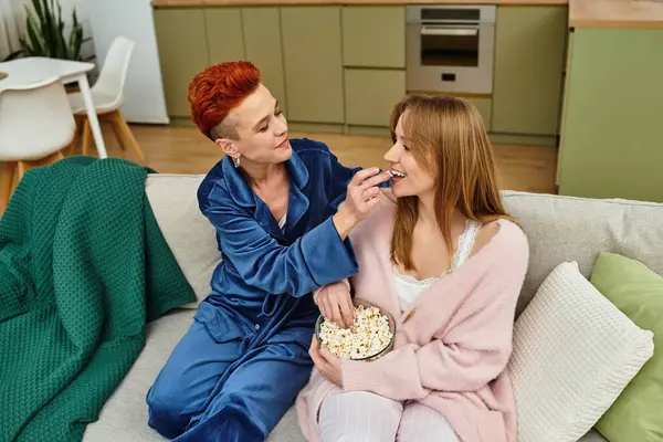 Two young women share a tender moment while enjoying popcorn in their modern apartment. — Stock Photo