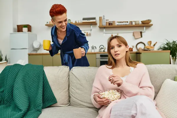 Two beautiful young women share a joyful moment in their stylish apartment, savoring popcorn. — Stock Photo