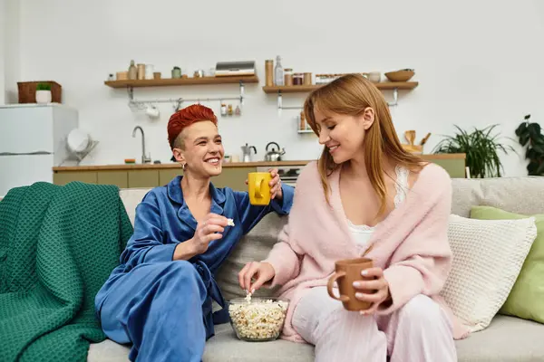 Two women share laughter and snacks while relaxing in their contemporary home setting. — Stock Photo