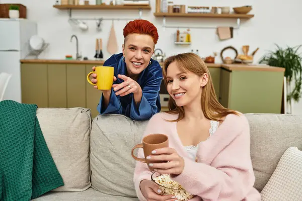 Two joyful young women enjoy each others company with warm drinks in their stylish home. — Stock Photo