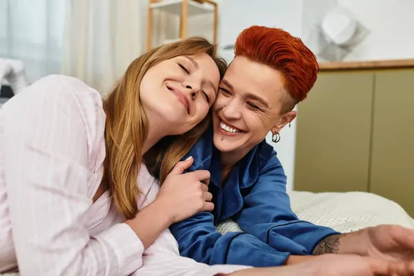 Due giovani donne gioiose si abbracciano nella loro accogliente camera da letto, irradiando amore e felicità insieme. — Foto stock