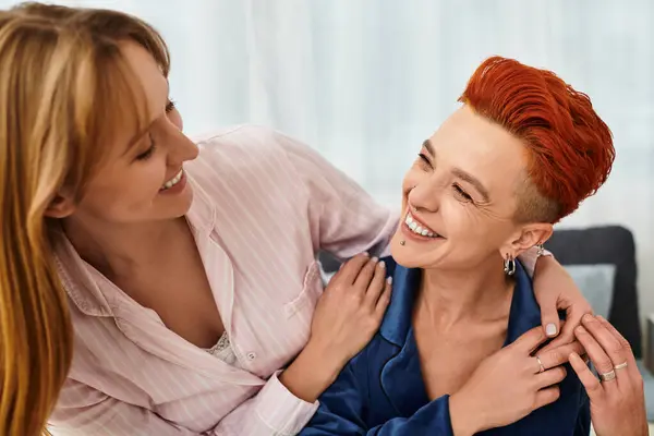 In una camera da letto luminosa, due giovani donne condividono caldi sorrisi e risate, abbracciando amore e gioia. — Foto stock