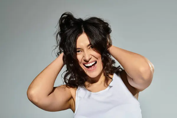 Captivating plus size woman brings joy in white tank top against grey background. — Stock Photo