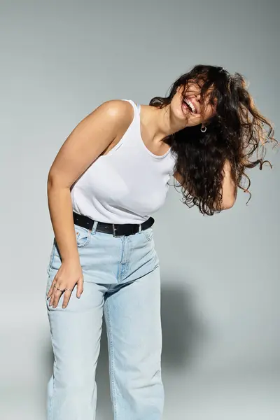 Plus size woman joyfully posing in a white tank top against a grey studio background. — Stock Photo