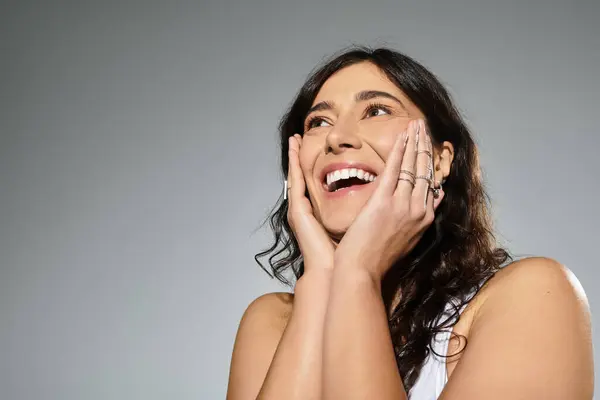 Smiling young plus-size woman in a white tank top on a grey background. — Stock Photo