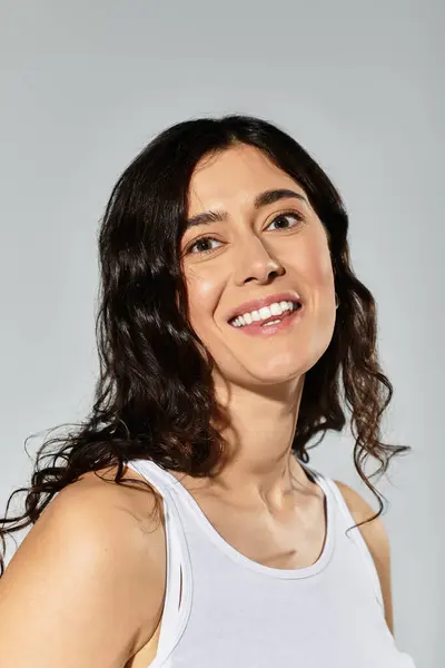 Brunette woman smiles confidently in a studio with a grey backdrop. — Stock Photo