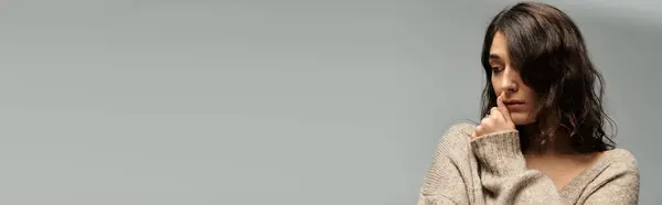 Young woman in casual attire poses thoughtfully against a grey backdrop. — Stock Photo